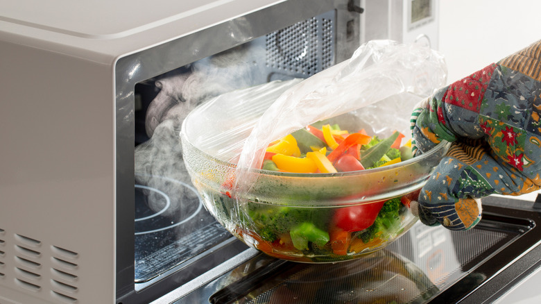 Removing steaming bowl of vegetables from microwave