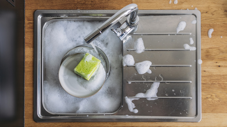 overhead view of dishes soaking in a small stainless steel sink, in sudsy water
