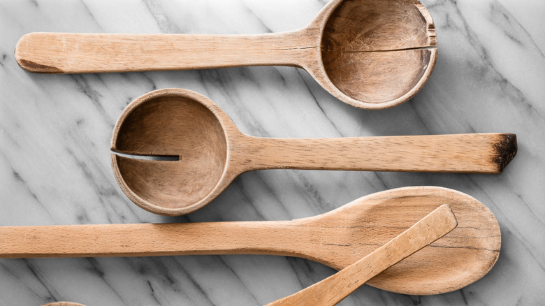three wooden spoons and the handle of another, all of the cracked and splitting, shown on a marble-look countertop