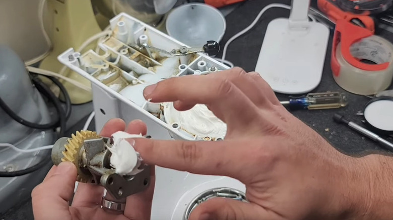 man's hands applying white grease lubricant to the gears of a vintage KitchenAid stand mixer