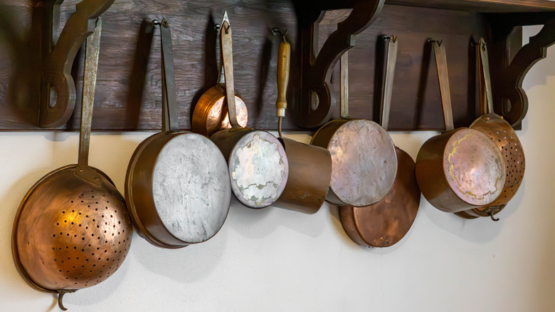vintage copper pots hanging from a rustic wooden wall rack