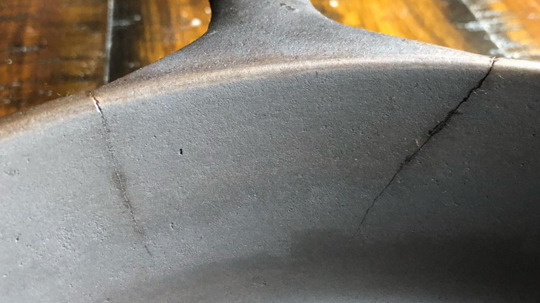 closeup of a cast iron skillet, with two severe cracks bracketing the handle of the pan