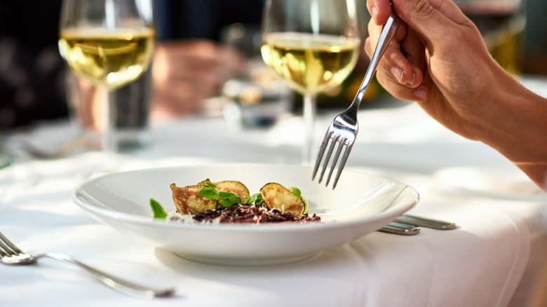 woman eating with a fork, food in a shallow bowl on white tablecloth