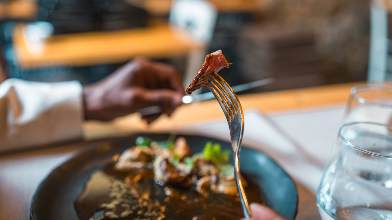 man holding a fork and steak knife while eating