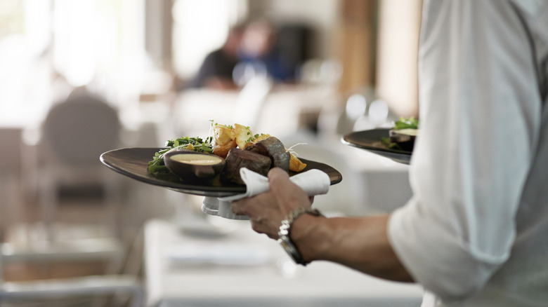 Waiter carrying plate of food to the table