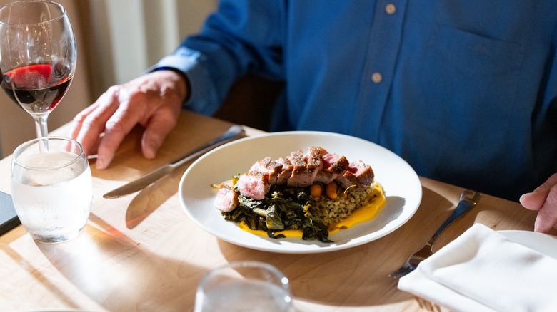 man with steak dinner, fork, knife, wine, and napkin on the table