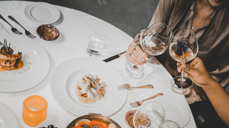 dinner table with two friends toasting wine glasses