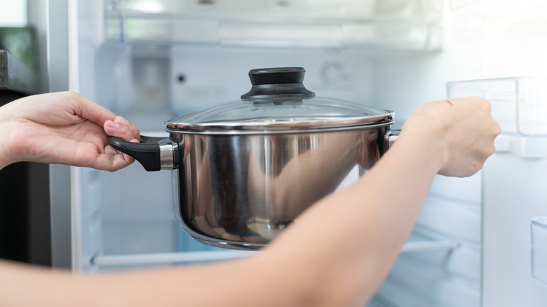 Person putting soup pot into refrigerator