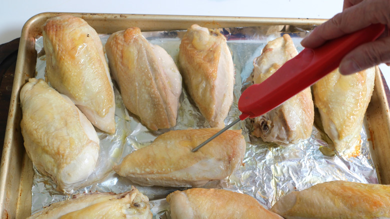 Person testing the temperature of chicken with meat thermometer