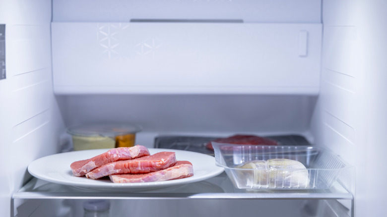 Plate of raw meat stored on refrigerator shelf