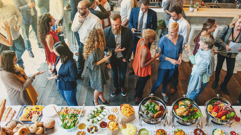 Various people mingling with drinks next to a buffet table