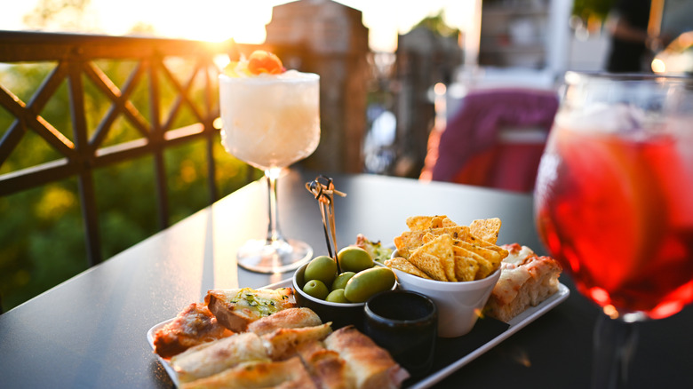 Pitcher and glass with cocktails and small plate of olive, chips, and rolls