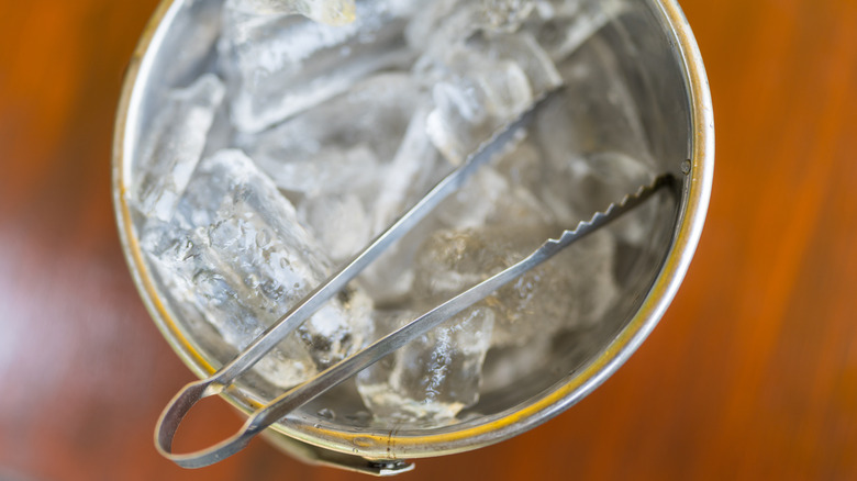 Metal bucket of ice with tongs