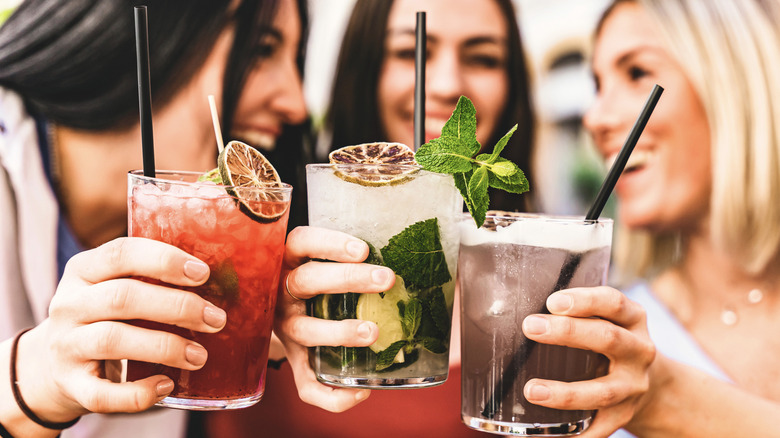 Three friends laughing and toasting with three different cocktails