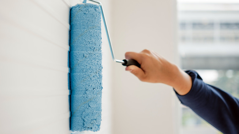 Person painting a white wall blue with a roller