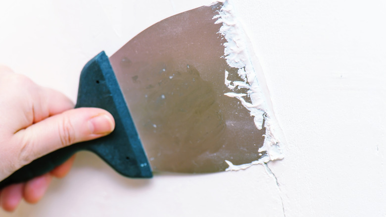 Hand filling in a wall crack with putty