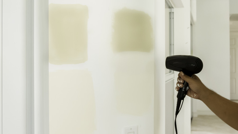 Hand holding a hair dryer to dry a painted wall quickly