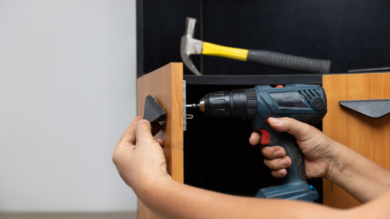 Person removing a cabinet handle with an electric drill
