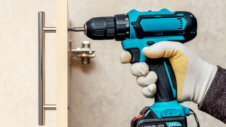 Hand using an electric drill to attach a handle to a door