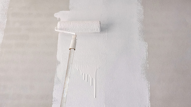 Painting white-colored primer on a wall with a long roller