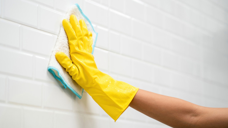 Hand wearing gloves to clean tiled walls with a rag