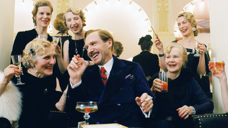 Monsieur Gustave surrounded by elegantly dressed women drinking cocktails in The Grand Budapest Hotel