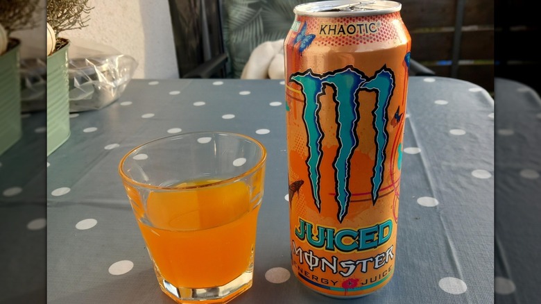 A can of Monster Juice Khaotic on a table next to a small glass of the beverage