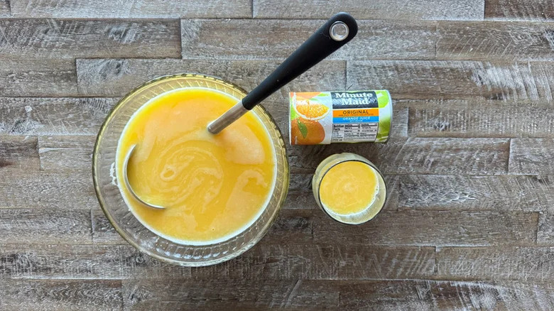 A can of frozen Minute Maid orange juice concentrate next to a bowl and glass of the prepared juice