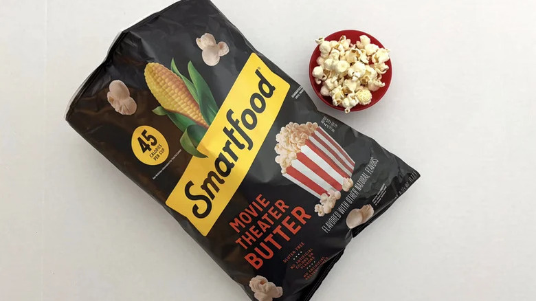 A bag of Smartfood Movie Theater Butter on a table next to a small red bowl of popcorn