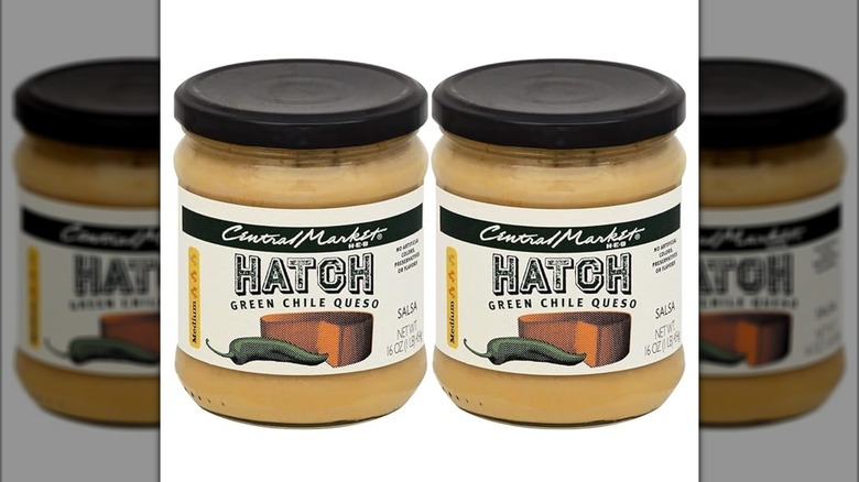 Two jars of Central Market Hatch green chile queso on a mirrored white background