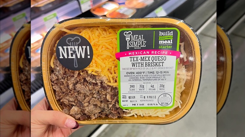 Top view of a hand holding a container of Tex-Mex brisket queso dip