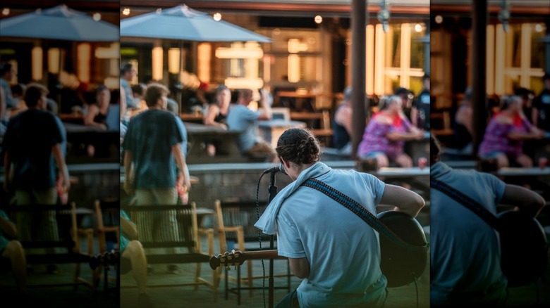 Guitarist sitting by microphone looking out at people in beer garden