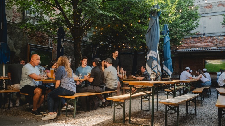 People at picnic tables outside under trees and lights