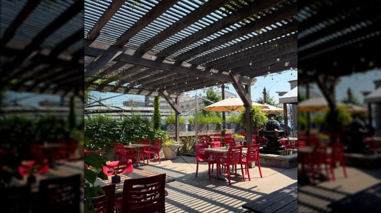 Outdoor patio with tables under a pergola and red chairs