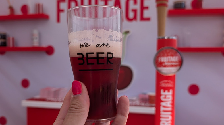 Manicured hand holding a tiny glass of fruity beer at London Craft Beer Festival
