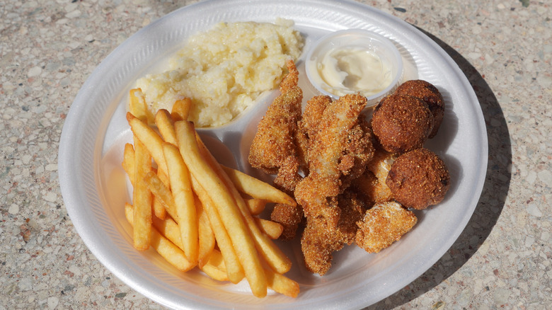 Fried catfish, grits, fries, and hush puppies on a styrofoam plate