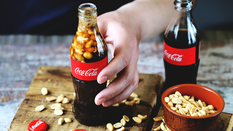 A hand holding a glass Coke bottle with roasted peanuts in and around it