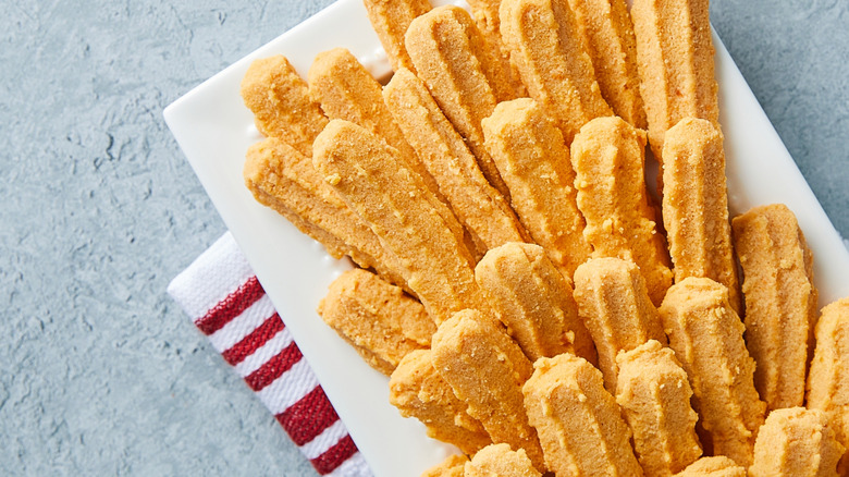 Crunchy Southern cheese straws on a white plate over a grey textured background