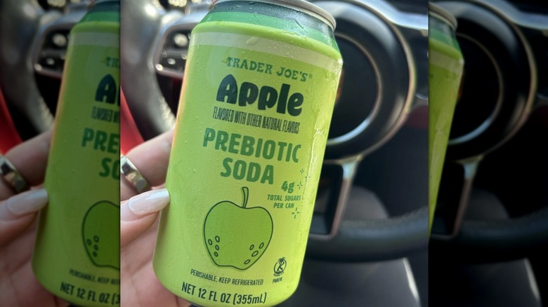 A person holding a green can of Trader Joe's Apple Prebiotic soda