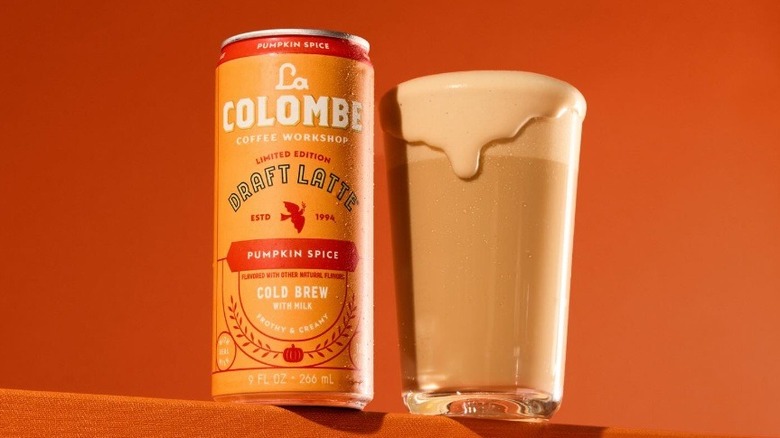 La Colombe Pumpkin Spice Cold Brew Latte can next to an overflowing glass on an orange background