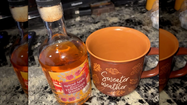 A part bottle of Trader Joe's Spiced Apple flavored Tennessee Whiskey next to a shot glass