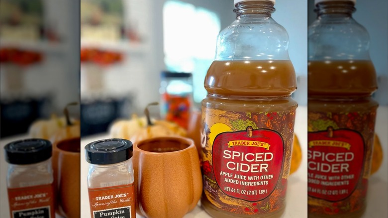 A bottle of Trader Joe's spiced cider sitting next to a mug and a container of pumpkin pie spice