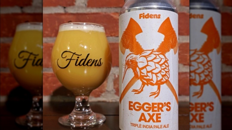 An orange and white can of Fidens Egger's Axe deer next to a full glass in front of a brick wall.