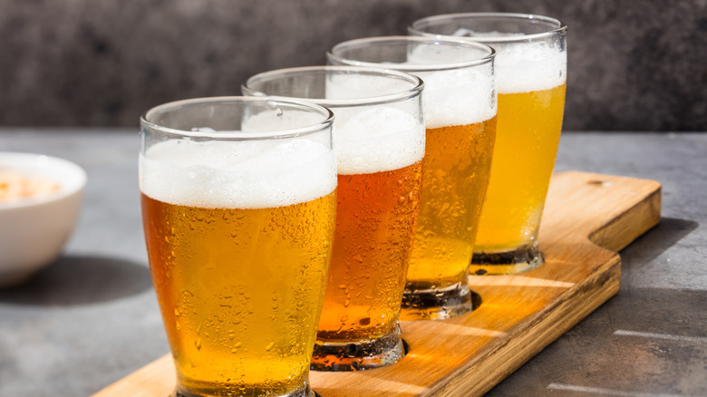 A flight of four IPA beers in condesnation-coated glasses on a wooden board.