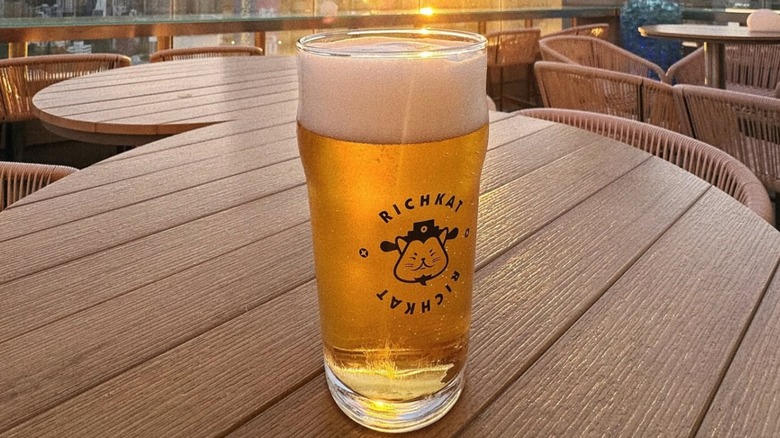 A full pint of Richkat beer on a patio table with a stylized cat logo on the glass.