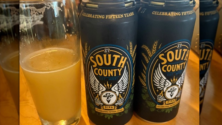 Two black cans of South County Brewing Co 15th Anniversary beer next to a half filled glass.