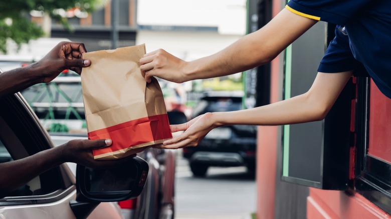 Fast food chain staff serving takeaway order for driver from delivery window