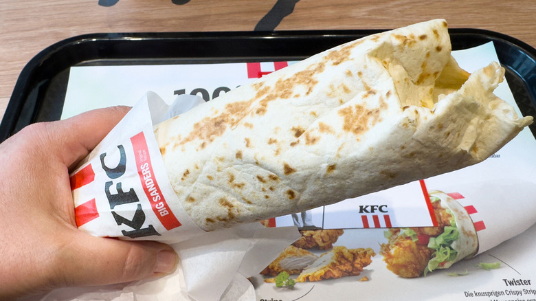 hand holding KFC wrap over tray