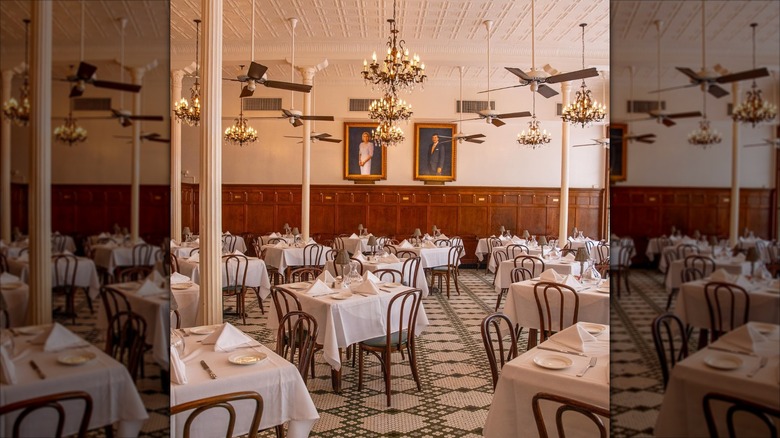 Elegant restaurant interior with white tablecloths, ceiling fans, chandeliers, skinny columns