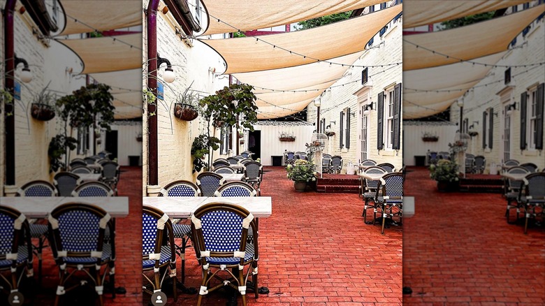 Exterior patio at Chez Billy Sud, white marble tables with blue and white chairs, tree on side